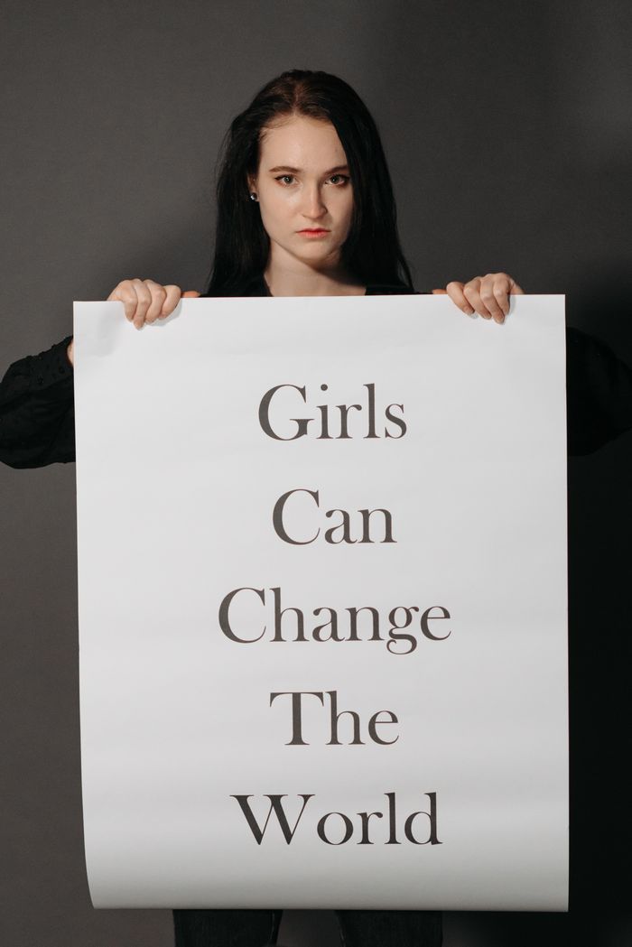 hero-img-02 A woman holds a powerful sign stating 'Girls Can Change the World' on a gray background.