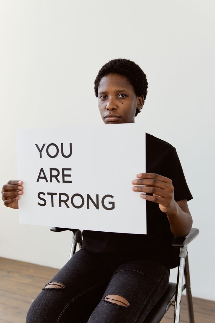 about-01 A portrait of a woman in a wheelchair holding a sign that reads 'YOU ARE STRONG,' promoting empowerment and resilience.