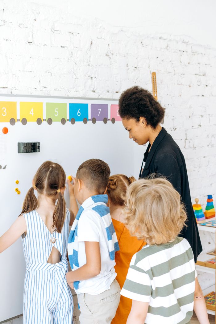 why-choose-us Children engaged in learning with a teacher at a colorful classroom whiteboard.